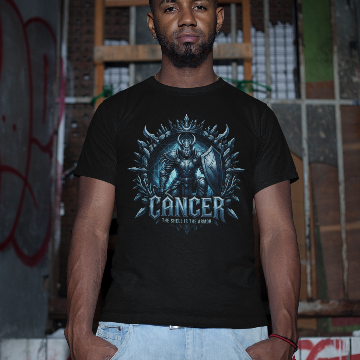 Male model with a short beard standing in a gritty, industrial basement setting wearing a premium black graphic streetwear t-shirt featuring a detailed chiseled metal Cancer shield warrior design by Essentia Collective.