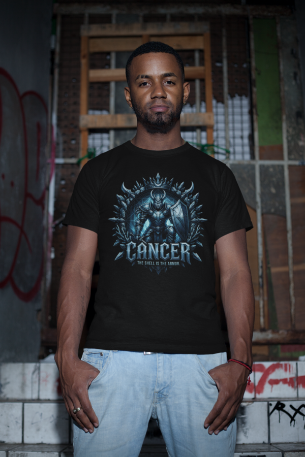 Cancer Shield Warrior Graphic Streetwear Black T-Shirt Male model with a short beard standing in a gritty, industrial basement setting wearing a premium black graphic streetwear t-shirt featuring a detailed chiseled metal Cancer shield warrior design by Essentia Collective.