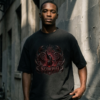 Male model standing against a weathered concrete alley wall in harsh daylight, wearing a premium oversized washed black streetwear t-shirt featuring a detailed red and metallic Scorpio archetype design by Essentia Collective.