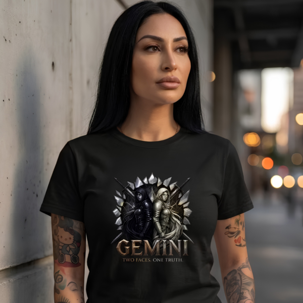 Tattooed female model with long straight dark hair standing against a concrete wall wearing a premium black graphic streetwear t-shirt featuring a detailed Gemini dual-warrior design by Essentia Collective.