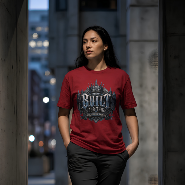 Built For This Urban Cardinal Red Streetwear T-Shirt Female model with long dark hair walking through a concrete urban passageway at dusk, wearing a cardinal red graphic streetwear t-shirt featuring a detailed gothic fortress Built For This design by Essentia Collective.