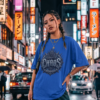 Chiseled By Chaos Graphic Royal Blue Streetwear T-Shirt Female model with braided hair and gold chains wearing black cargo pants, standing in a rainy neon-lit Tokyo street at night while wearing an oversized blue graphic streetwear t-shirt with a Chiseled By Chaos design by Essentia Collective.