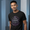 male model standing in front of light blue and slate gray abstract geometric pillars, wearing a premium black graphic t-shirt with a metallic purple and silver celestial crest reading In My Zodiac Healing Era.