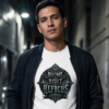 Male model wearing a white Essentia Collective t-shirt under a black bomber jacket, featuring a black gothic graphic reading Restart Reset Refocus, set in a dark urban alleyway.