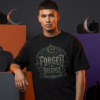 Male model standing in a dark creative studio environment with geometric orange and purple accent blocks, wearing a premium black graphic streetwear t-shirt with a detailed silver and bronze Forged In Silence emblem design.