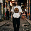 Female model wearing a green beanie, a thick silver chain necklace, black oversized cargo pants, and a premium white graphic streetwear t-shirt featuring a roaring golden Leo lion design by Essentia Collective walking down a dark, wet urban alleyway at night.