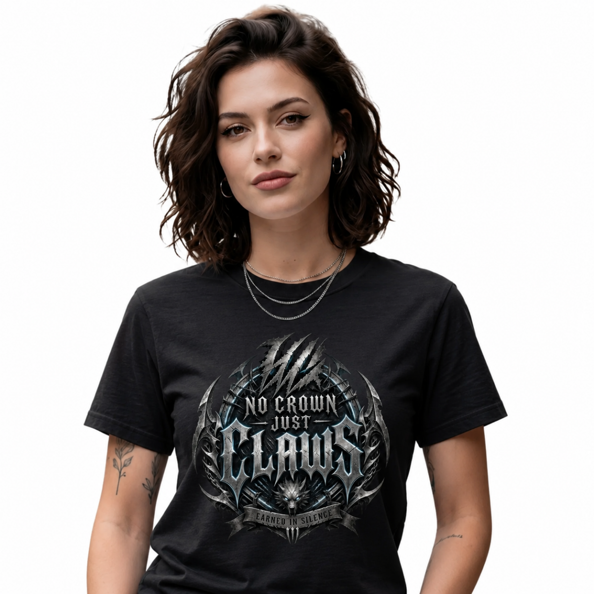 female model with short wavy brown hair on a clean white background, wearing a black Essentia Collective graphic tee featuring a detailed silver and blue metallic gothic chest graphic reading No Crown Just Claws.