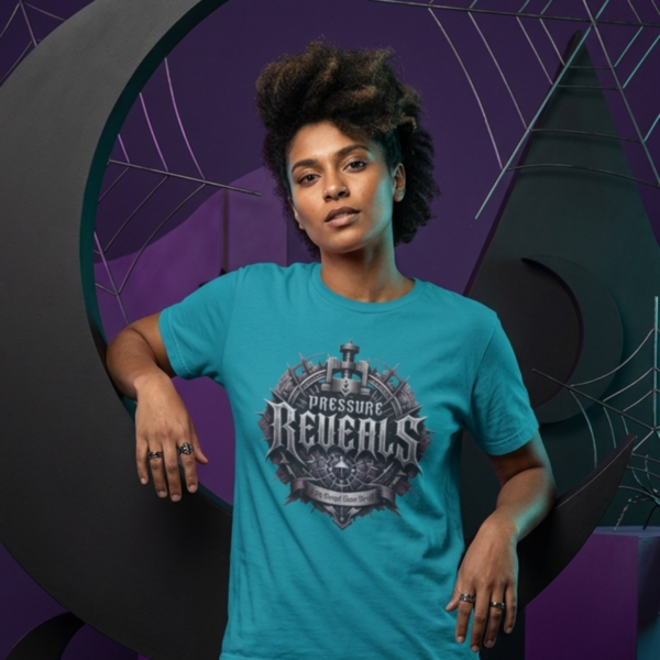Pressure Reveals Streetwear T-Shirt Tropical Blue female model with an afro standing in a dark alternative studio in front of an orange geometric box and black crescent moon, wearing a teal blue Essentia Collective graphic t-shirt with a metallic gothic crest that reads Pressure Reveals.