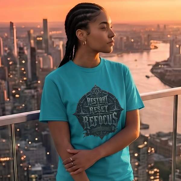 Female model with braided hair wearing a teal blue Essentia Collective t-shirt with a detailed emblem reading Restart Reset Refocus, standing on a balcony overlooking a city skyline at sunset.