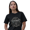 Studio product mockup of a female model with dark hair and hoop earrings, wearing a black premium Essentia Collective graphic t-shirt featuring a silver gothic emblem with claw marks reading Scars Louder Than Fear.