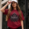Low Profile Gothic Style Cardinal Red Streetwear T-Shirt Female model with long brown hair wearing a white baseball cap, standing in front of an ornamental dark wrought iron gate while wearing a vibrant red graphic streetwear t-shirt with a detailed black and silver Low Profile emblem design.