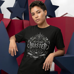female model with short cropped dark hair leaning against large blue and red geometric star structures, wearing a black premium Essentia Collective graphic streetwear t-shirt with a detailed silver gothic emblem reading Nothing Wasted.