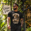 Male model wearing a black Scorpio graphic T-shirt in a sunlit urban setting surrounded by greenery.